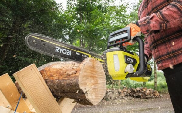 En person håller i en RYOBI kedjesåg RY36CSX40B-0 och sågar i en stock med träd i bakgrunden